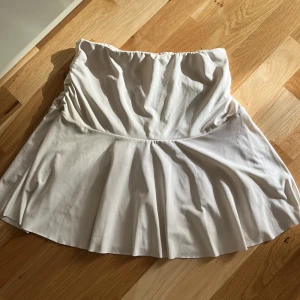 Vit kjol - Supersöt vit kjol med snygg rynkdetalj på sidorna. Kjolen har en lätt utsvängd och är gjord i ett mjukt, slätt material som känns skönt mot huden. Perfekt för sommarens alla tillfällen! Tyvärr är den lite missfärgad vid vissa ställen, som vid ena rynkdetaljen