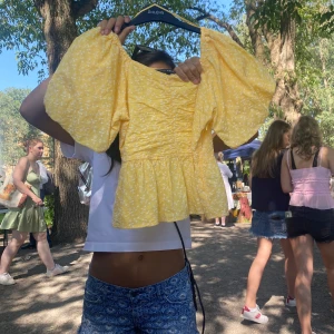 Gul blommig blus med puffärmar - Supersöt gul blus med små vita blommor och stora puffärmar. Toppen har fyrkantig ringning, rynkade detaljer framtill och en volang nertill som ger en flowy känsla. Perfekt för soliga dagar och ger en riktigt somrig vibe!