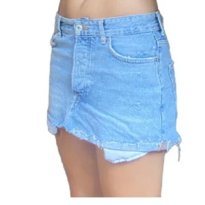 Ljusblå jeanskjol från Bershka - Säljer en ljusblå jeanskjol från Bershka Vintage Collection. Kjolen är kort med råa, fransiga kanter och klassiska fickor både fram och bak. Perfekt för dig som gillar en avslappnad och trendig denimlook.