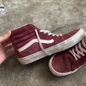 Vinröda Vans Sk8-Hi sneakers mocka - Säljer ett par klassiska Vans Sk8-Hi sneakers i vinröd mocka med vit sula och vit ikonisk sidostrip. Högt skaft, vita skosnören och vadderad insida för extra komfort. Perfekta för dig som gillar streetstyle och vill sticka ut med färg.🍇