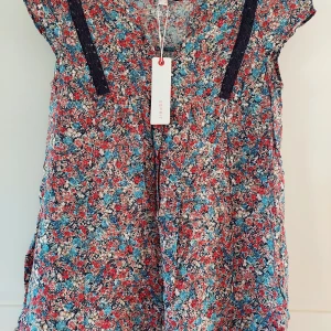 Blommig kortärmad blus från Esprit - Supersöt blus från Esprit med blommigt mönster i rött, blått och vitt. Blusen har v-ringning, korta ärmar och dekorativa mörkblå spetsdetaljer framtill. Perfekt för dig som gillar färg och mönster!