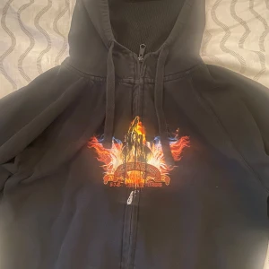 Sweden Rock Festival hoodie 2012 - Svart hoodie med dragkedja från Sweden Rock Festival 2012. Grym festivalprint med eld och bandnamn på bröstet samt stor line-up på ryggen. Huva med snörning och mjukt material i bomull och polyester. Perfekt för dig som älskar rock och vill sticka ut.