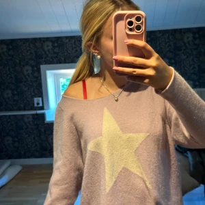 Ljuslila stickad tröja med stjärna Hunkydory - Supermjuk ljuslila stickad tröja från Hunkydory med stor vit stjärna framtill. Tröjan har en loose passform och bred halsringning som kan bäras offshoulder. Perfekt för dig som gillar en chill och trendig vibe.