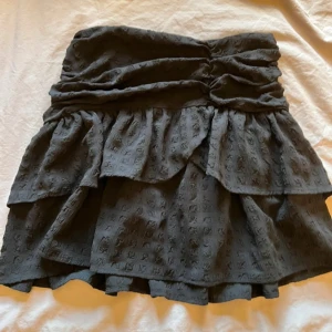 Svart volangkjol med struktur - Supersöt svart kortkjol med volanger och snygg struktur i tyget. Kjolen har en medelhög midja men går även att använda low, med rynkade detaljer och ett unikt mönster i materialet. Perfekt för dig som vill ha en trendig och bekväm look. Skriv vid intresse, storlek M men passar även S använd fåtal gånger från Gina tricot!💕🙌