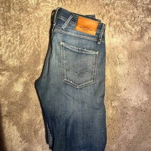 Replay Anbass blå jeans herr - Säljer ett par Replay Anbass jeans i klassisk blå tvätt med snygga slitningar och detaljer på bakfickorna. Modellen har en slim passform och raka ben, med läderpatch bak i midjan. Perfekta för dig som gillar en modern och avslappnad stil.