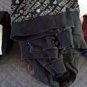 Svart hoodie från Vans med tryck - Svart hoodie från Vans med coolt vitt texttryck 'Off The Wall' över hela framsidan. Tröjan har huva och långa ärmar med breda muddar. Perfekt för dig som gillar streetwear och vill ha en chill look.