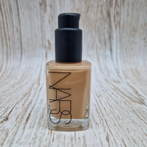 NARS Sheer Glow Foundation Vanuatu - Säljs billigt för att lock och förpackning saknas. NARS Sheer Glow Foundation i nyansen Vanuatu (Medium 3.5) med en naturlig, varm beige ton. Kommer i en stilren glasflaska med svart pump och rymmer 30 ml. Perfekt för dig som vill ha en lätt, glowig finish och jämn hudton.