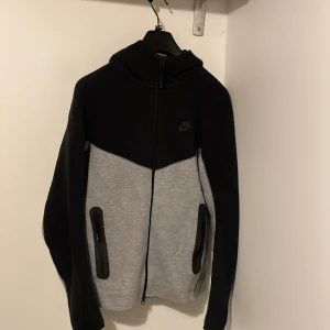 Nike hoodie svart och grå S - Nike hoodie i svart och grått med hel dragkedja och huva. Tröjan har två fickor med dragkedja på framsidan och en stilren design med svart övre del och grå nedre del. Perfekt för chill eller träning, mjukt material och långärmad. Pris går och diskutera
