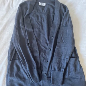 Mörkgrå kofta från COS - Snygg mörkgrå kofta från COS med klassisk design och fyra knappar framtill. Bra kondition - Storlek S