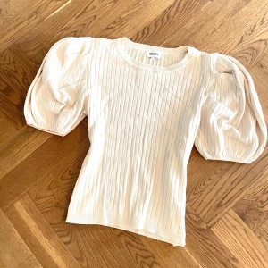 Beige ribbad topp med puffärm - Supersnygg ribbad topp med puffiga kortärmar som ger en trendig siluett. Rund halsringning och stretchigt material som sitter skönt. Perfekt att styla med jeans eller kjol för en cool look.
