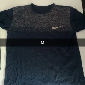 Mörkblå Nike t-shirt med mönster - Snygg mörkblå t-shirt från Nike med korta ärmar och coolt mönster upptill i vitt och grått. Materialet känns lätt och passar perfekt för träning eller chill. Nike-loggan syns tydligt på bröstet. Klassisk rund hals och normal passform.