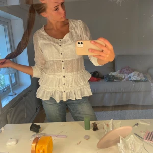 Vit volangskjorta med spetsdetaljer - Supersöt vit skjorta med volanger och spetsdetaljer, knappar framtill och lätt transparent material. Skjortan har en feminin v-ringad hals och trekvartsärmar. Perfekt för dig som gillar romantisk och boho-inspirerad stil.