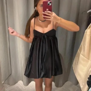 Svart satin klänning  - Slutsåld! Endast använd på nyår!! Supersnygg svart kortklänning i glansigt satinmaterial med tunna axelband och voluminös kjol. Klänningen har en söt, ballongformad siluett och markerad byst. Perfekt för dig som vill ha en chic och trendig look.