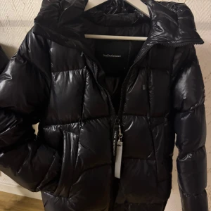 Svart pufferjacka Peak Performance XS - Säljer en svart pufferjacka från Peak Performance i storlek XS. Jackan har en glansig finish, huva, två sidofickor och dragkedja framtill med Peak Performance-nyckelring. Perfekt för kalla dagar och har en schysst, lite oversized look.