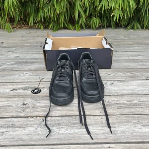 Nike Air Force 1 Low ’07 Fresh Black Anthracite - Nike Air Force 1 sneakers i helsvart färg med klassisk låg siluett. Skorna har en rund tå, platt sula och är tillverkade i skinn med snygga sömdetaljer och perforeringar på tån. Swoosh-logga på sidan och AIR-märkning på hälen. Perfekt för dig som gillar stilrena och tidlösa kicks.                                                                                Skorna är knappt använda och är äkthetsverifierade av sneak.se. Skorna kostar ungefär 2500kr helt nya.
