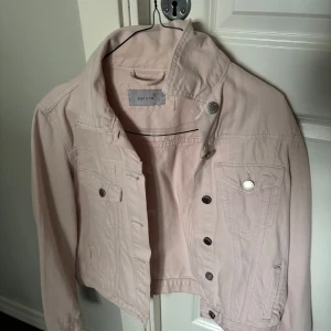 Ljusrosa jeansjacka från Per Una - Snygg ljusrosa jeansjacka från Per Una med klassisk krage, silverfärgade knappar och två bröstfickor. Jackan har en croppad passform och är tillverkad i bomull. Perfekt att slänga över en t-shirt för en chill look.