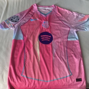 FC Barcelona x Nike rosa fotbollströja - Snygg FC Barcelona fotbollströja från Nike i rosa och ljusblå toner med tunna vita ränder. Tröjan har korta ärmar, klubbmärke på bröstet, Spotify-logga och UEFA Foundation-märke på ärmen. Tillverkad i lätt, ventilerande polyester för max komfort på planen. Använd 1 gång, Pris kan diskuteras 