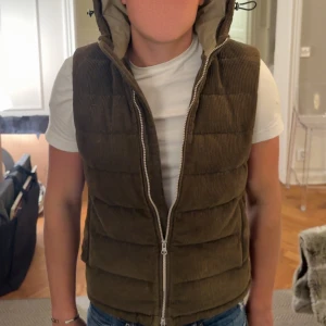 Stenströns | Brun quiltad dunväst med huva - Säljer en brun/grön stenströms dunväst med breda quiltade paneler och en stor, vadderad huva. Västen är gjord i manchestertyg och har en rejäl dragkedja framtill. Perfekt att slänga över en hoodie eller t-shirt för extra värme. Väldigt bra skick och storlek M