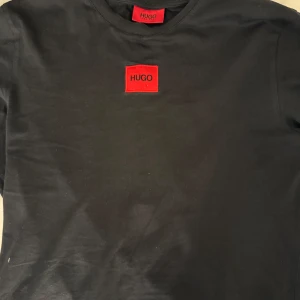 Hugo boss T-shirt  - Säljer en svart hugo boss T-shirt med röd logga, T-shirten är i storlek s men passar även m. I bra skick och knappt använd. Nyköpt för 580kr!