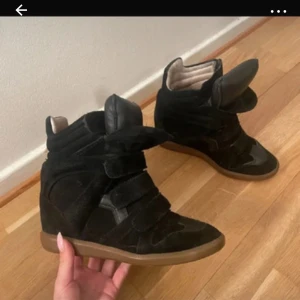 isabel marant skor, storlek 37 - Säljer ett par svarta sneakers från Isabel marant i storlek 37. Skorna har kilklack, rund tå och flera breda kardborreband över foten. Ovandelen är i mocka och skinn, med en brun gummisula som ger cool kontrast. Perfekt för dig som gillar chunky och edgy stil.