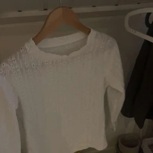 Vit blus med spetsdetaljer, stl S - Supersöt vit blus i storlek S med lång ärm och broderade spetsdetaljer. Blusen har ett mönster av små hål och zigzag-linjer, vilket ger en romantisk vibe. Tillverkad i mjuk polyester med lite stretch för skön passform.