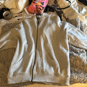 Grå hoodie med dragkedja från Bik Bok - Säljer en enkel och chill grå hoodie från Bik Bok i storlek XS. Den har dragkedja hela vägen, två fickor fram och en skön huva. Perfekt för att slänga på sig när det är lite kyligt ute. Materialet är mjukt och känns som bomull.