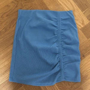 Blå ribbad kjol från Zara - Supersnygg blå kortkjol från Zara i ribbat material. Kjolen har en tight passform och cool rynkdetalj framtill. Jag har även använt den som en topp någon gång! Super snygg men tyvärr inte min stil längre