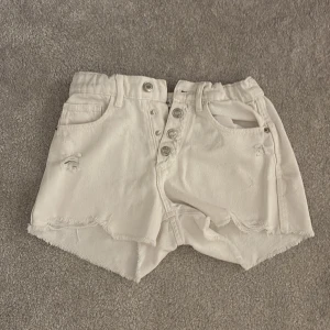 Vita jeansshorts från Zara - Snygga vita jeansshorts från Zara med hög midja, råa kanter och slitna detaljer. Shortsen har flera fickor, knappstängning framtill och ett klassiskt jeansmärke bak. Perfekta för sommarens chill dagar och har en loose passform.