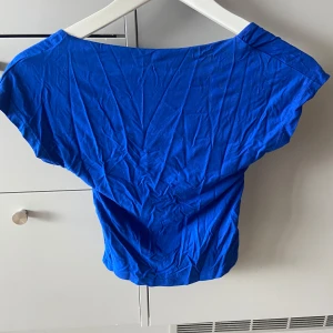 Blå croppad topp med öppen rygg - Snygg blå croppad topp med bred halsringning och öppen rygg. T-shirten har korta ärmar och är gjord i mjukt bomullsmaterial. 