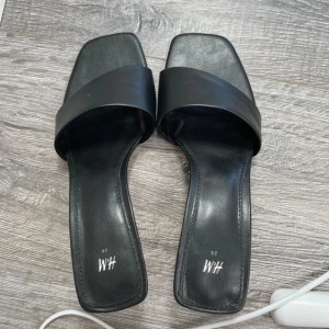 Svarta sandaler med fyrkantig tå - Snygga svarta sandaler från hm med bred rem över foten och trendig fyrkantig tå. Platt sula och minimalistisk design som passar perfekt till jeans eller klänning. .Jätte fina klackar som passar perfekt till en utekväll, strl 36, jag har 36-37 i storlek som referens på bilden. Helt nya!