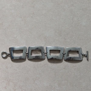 Stilrent armband i silverfärg - Snyggt armband med fyra rektangulära länkar i silverfärgad metall. Länkarna har en öppen design och armbandet stängs med en klassisk stavlås. Perfekt för dig som gillar minimalistisk och modern stil.