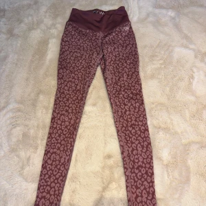 Leopardmönstrade leggings från DOM - Snygga mörkrosa leggings från Drop of Mindfulness med leopardmönster. Hög midja och stretchigt material i polyester och elastan gör dem perfekta för träning eller chill. De har en smickrande passform och coolt DOM-tryck vid linningen.