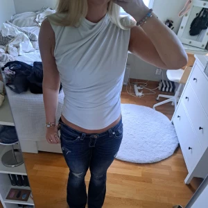 Vit topp från Zara - Säljer en vit omlott topp från Zara i storlek S. Toppen har ärmlös design och coola draperade detaljer över axel och midja som ger en snygg siluett. Materialet är mjukt och stretchigt, perfekt för att styla med jeans eller kjol. Slut i lagret på zara.