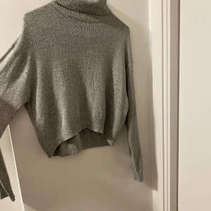Grå high neck tröja från H&M Divided XS - Snygg grå polotröja från H&M Divided i storlek XS. Tröjan är stickad med mjukt material och har en hög polokrage samt långa ärmar. Passformen är loose och den har en lite croppad look med ribbade muddar. Perfekt för att hålla sig varm och stilren.
