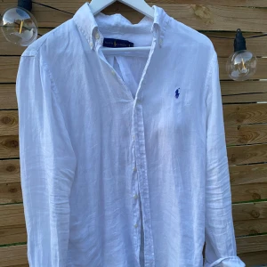 Vit linneskjorta från Ralph Lauren - Vit skjorta i linne från Ralph Lauren med klassisk krage och blå broderad logga på bröstet. Långärmad modell med knappar framtill och vid manschetterna. Luftig och stilren, perfekt för varma dagar. Snyggt avslappnad passform. Vid frågor eller funderingar skicka gärna ett meddelnade!🙌💫