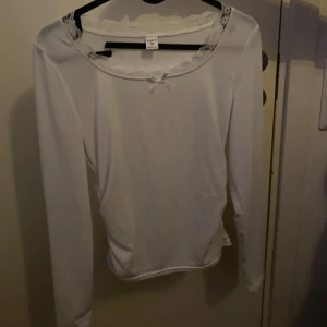 Vit långärmad topp med spets från Shein - Säljer en vit långärmad topp från Shein med söt spetsdetalj runt halsringningen och en liten rosett framtill. Toppen har en slim passform och är tillverkad i mjuk bomull, perfekt för dig som gillar enkla men fina detaljer. Använd några gånger men inget som är fel på den 🩵
