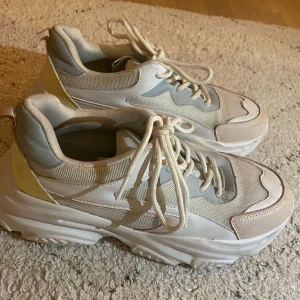 Vita sneakers - Säljer ett par chunky sneakers från Ivy i vitt och beige med inslag av ljusgrått. Skorna har plattformssula, rund tå och snörning. Ovandelen är i mesh och syntet, vilket ger en cool och sportig vibe. Perfekta för dig som gillar streetstyle och vill sticka ut.
