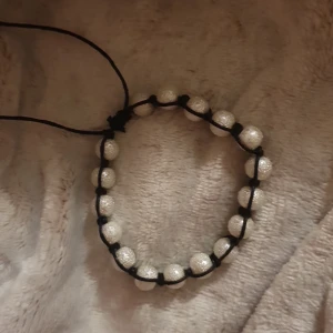Svart armband med glittriga pärlor - Snyggt handgjort armband med svarta snören och glittriga vita pärlor. Pärlorna är jämnt fördelade och sitter fast med knytning, vilket ger en cool och trendig look. Perfekt accessoar för att lyfta din outfit med lite extra bling.