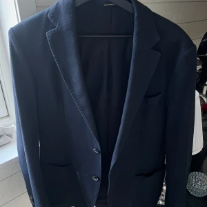 Marinblå kavaj från Massimo Dutti - Snygg marinblå kavaj från Massimo Dutti i extrafin bomull. Klassisk modell med två knappar framtill, tre knappar vid ärmslut och diskreta fickor. Tyget har en lätt strukturerad yta som ger en modern känsla. Perfekt för dig som gillar stilrena plagg.