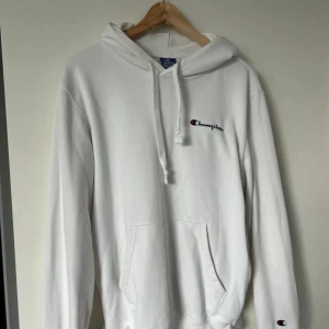 Vit hoodie från Champion i medium - Säljer en clean vit hoodie från Champion i storlek medium. Tröjan har huva med snörning, känguruficka och broderad Champion-logga på bröstet och ärmen. Materialet är mjukt med 67% bomull och 33% polyester, perfekt för chill dagar.
