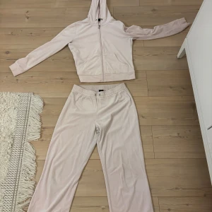 Ljusrosa sätt från Gina tricot  - Supermjukt ljusrosa set i velour med dragkedja framtill och huva. Tröjan har långa ärmar och två fickor framtill. Perfekt för en chill och avslappnad stil. 