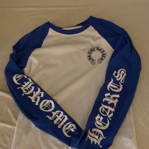 Chrome Hearts långärmad tröja blå/vit - Säljer en långärmad tröja från Chrome Hearts i storlek S. Tröjan är vit med blå ärmar och blå detaljer vid halsen. Stora tryck på ärmarna och ryggen, samt Chrome Hearts-logga på bröstet. Tillverkad i bomull och har en riktigt streetig vibe. printen på vissa ställen kom bort i tvätten 