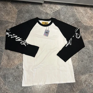 Corteiz Guerillaz svartvit långärmad tröja - Snygg långärmad tröja från Corteiz Guerillaz i svart och vitt. Tröjan har svartvita raglanärmar med tryck på ärmarna och broderad logga på bröstet. Tillverkad i mjuk bomull, perfekt för en chill streetwear-look.