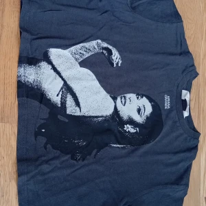Svart Ariana Grande t-shirt från H&M - Cool svart t-shirt från H&M med stort vitt tryck av Ariana Grande på framsidan. Klassisk rund hals och korta ärmar. Perfekt för dig som älskar musik och vill sticka ut med en snygg och bekväm tee i bomull.
