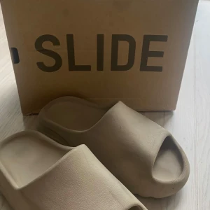  beiga yeezy slides -  🍂 Yeezy Slides – Perfekta för Höstmyset! 🍂  Säljer ett par snygga och bekväma Yeezy Slides i den populära beige färgen. Dessa är perfekta för hösten och vintern!  *   Storlek: US 5 (vilket motsvarar ungefär storlek 37 i EU). *   Skick: Helt nya och oanvända. *   Äkthet: 100% äkta, garanterat! *   Ingår: Originalkartong medföljer.  Unna dig själv eller någon du tycker om dessa ikoniska slides. De är lika snygga som bekväma! det står att de är 38 men de är ganska så små i storleken🌟