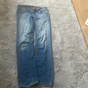 Blå jeans från Kaporal med broderi - Säljer ett par snygga blå jeans från Kaporal med coolt broderat Kaporal-logo på baksidan. Jeansen har klassisk femficksdesign, kontrastsömmar och slitningar för en avslappnad vibe. Passformen är inte bootcut men inte skinny. Dom är från 2004 då det är min mammas gamla jeans. Men är i väldigt bra skick. Skulle säga att storleken är w23