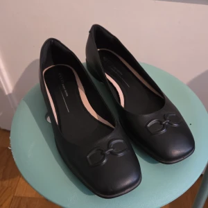 Svarta ECCO ballerinaskor i skinn - Stilrena svarta ballerinaskor från ECCO i mjukt skinn med fyrkantig tå och diskret dekordetalj framtill. Platt sula och klassisk design som passar perfekt till både jeans och kjol. Skorna har en bekväm innersula och är lätta att bära hela dagen.