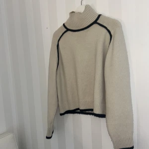Beige polotröja med svarta detaljer H&M - Säljer en beige polotröja från H&M i storlek S. Tröjan är stickad med svarta kontrastdetaljer längs sömmarna, muddar och krage. Den har lång ärm, ribbad polokrage och en loose fit. Knappt använd max 3-4gnr och tvättad 1 gång