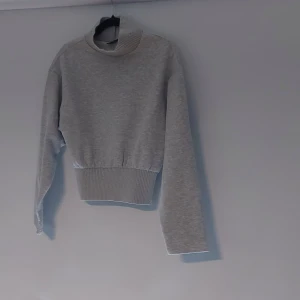 Grå polotröja från Gina Tricot - Supermjuk grå polotröja från Gina Tricot med bred ribbad mudd i midjan och vid kragen. Tröjan har lång ärm och en clean, enkel look som är lätt att matcha. Perfekt för lager-på-lager och chill vibes.