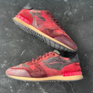 Valentino Garavani Rockrunner sneakers röd - Snygga Valentino Garavani Rockrunner sneakers i rött och vinrött med coolt kamouflagemönster. Skorna har detaljer i mocka, skinn och textil samt ikoniska nitar på hälen. Perfekta för dig som vill sticka ut med exklusiva och trendiga sneakers. Bara skriva om mer info och bilder🤩